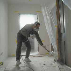A worker in protective gear painting walls during an indoor renovation project.
